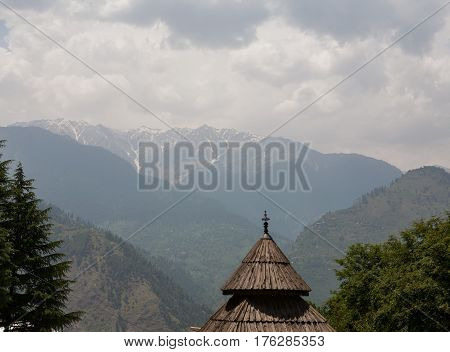 MANALI, INDIA. The wooden roof of the Tripura Sundari Temple on the backdrop of Himalayas on a cloudy day. Naggar, district Kullu in Himachal Pradesh, India.