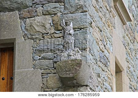 Sculpture of angel defeating the enemy on the background of a stone building in Rupit (Catalonia Spain)
