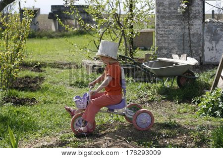 Cute girl playing outdoors with a bike and an old bucket helmet
