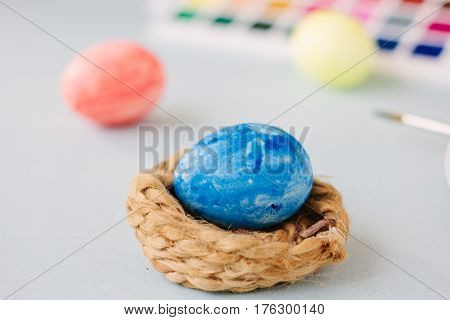 Deep Blue Easter Egg On Nest Over Bright Background.