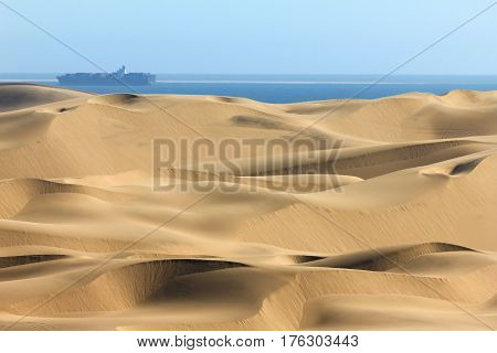 Sand dune desert meets water of the Atlantic Ozean. Container ship on the water.