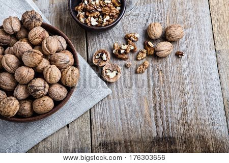 on a wooden table is a plate with walnut in thair shell beside it are cracked nuts and shells. the plate is stnding on the linen napkin.