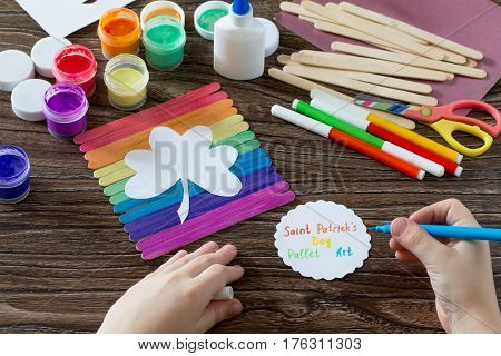 The Child Draws The Details. Present For St. Patrick's Day Clover On A Rainbow, A Craft Of Of Wooden
