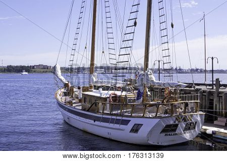 Halifax, Nova Scotia September 23 2015 -- Wide view of a wood trimmed sail boat docked at the Halifax Harbor on a beautiful bright sunny day in September with Dartmouth buildings in the background in Halifax, Nova Scotia