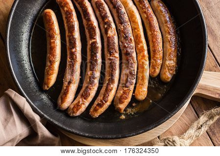 Variety of fried or roasted sausages with appetizing golden crust in iron cast pan wood kitchen table top view