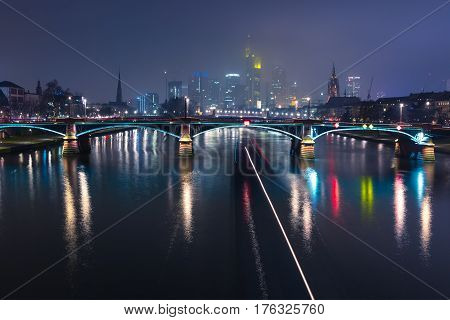Picturesque view of Frankfurt am Main skyline and Ignatz Bubis Brucke bridge during evening blue hour with mirror reflections in the river, Germany