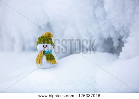 Snowman the Santa's assistant is standing in green hat wrapped with the scarf on nice textured snow on frosty winter morning.