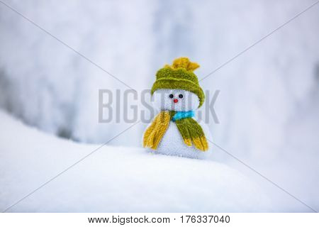 On the white fluffy textured snow alone snowman the friend is standing in nice hat and scarf with red nose.