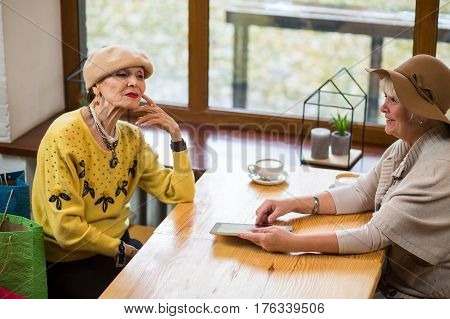 Elderly women and a tablet. Cafe table near window. Friends discuss new technologies.