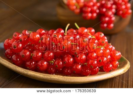 Raw red currants (lat. Ribes rubrum) on plate photographed on dark wood with natural light (Selective Focus Focus one third into the redcurrants)