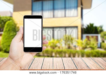 Mock up image of hand holding black mobile phone with blank white screen Empty wood table top on blurred images home garden for background perspective wood can be used for display products.