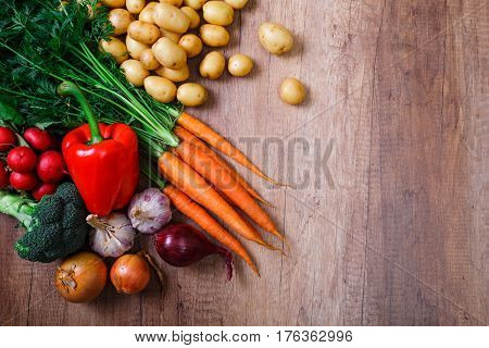 Potatoes with carrot, garlic and pepper. Red radish, brocoli and raw new potato. Onion. Fresh natural vegetables. Organic bio food. On wooden table.