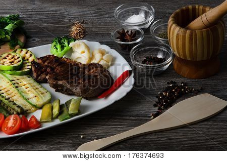 Grilled beef grilled with asparagus, zucchini, lobi, broccoli, tomato, chili and red sauce on a white plate, and other vegetables in wood background