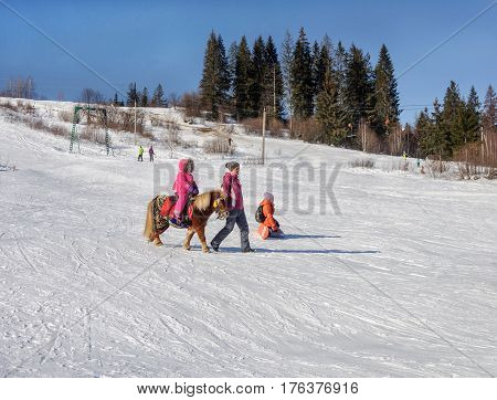 Slavske Ukraine - January 30 2017: Ski resort Slavske in Carpathians. Little girl riding pony on mountain slope. Sunny winter day.