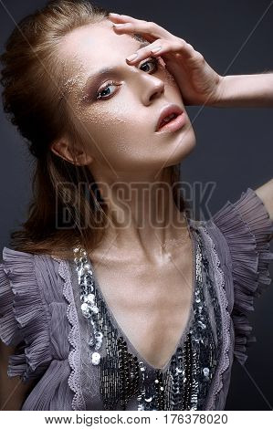 Young girl with creative makeup and textures on her face. Beautiful model in a lilac dress with sparkles. Photo is taken in the studio. Beauty of the face.