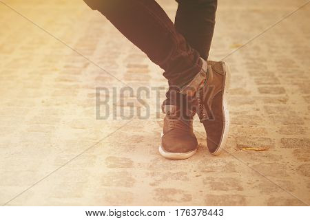 Close-up picture of man who crossed his legs. Man in black jeans and sneakers enjoying daytime in the city. Toned image.