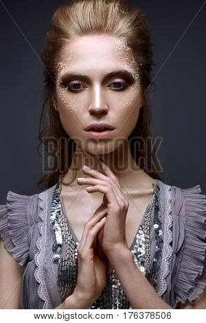 Young girl with creative makeup and textures on her face. Beautiful model in a lilac dress with sparkles. Photo is taken in the studio. Beauty of the face.