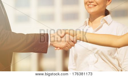 Handshake with businesswoman at backdrop showing business partnership. Man and woman have singed lucrative contract. Toned image.