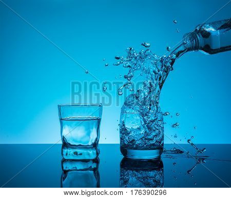 Bottle with creative splashing water in the glass on blue background.