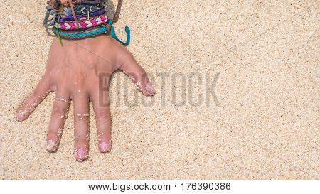 Women Hand with Colourful Wristband Toching Wet Sand on the Beach. Vertical orientated