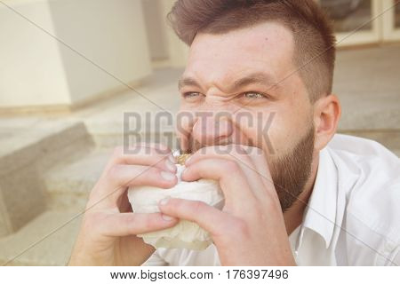 Close-up portrait of insatiable and hungry man eating cheeseburger. Bearded man having a snack during his lunch time. Toned image.
