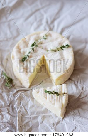 Block of brie cheese on wrapping paper with thyme herbs