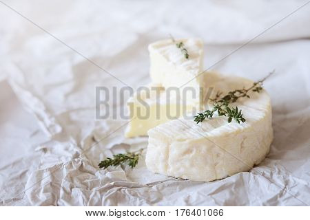 Block of brie cheese on wrapping paper with thyme herbs
