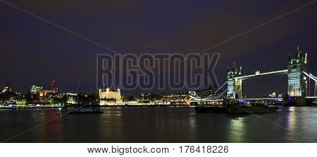 Night time panorama of Tower Bridge spanning the River Thames with Tower of London in the distance.  London, England 2017