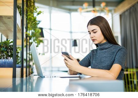 Young beautiful woman wearing glasses working in the office uses a laptop and mobile phone