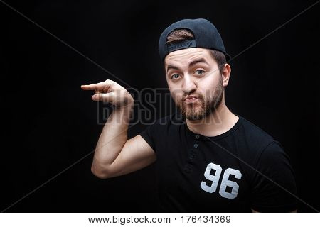 handsome man with beard pointing copy space. young man in t-shirt looking at camera and pointing away against black background