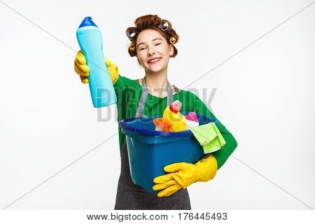 Beautiful housewife holds cleaning tools and shows bottle with wide smile arter busy day