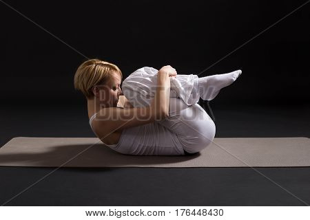 Woman exercising yoga indoor on black background,Wind Relieving pose/Pawanmuktasana
