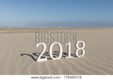 White wood figures on a beach forming the text two thousand eighteen as conceptual welcoming of the coming new year