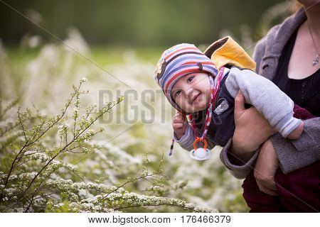 Little Boy Smiles At The Background Of Flowers In The Park.