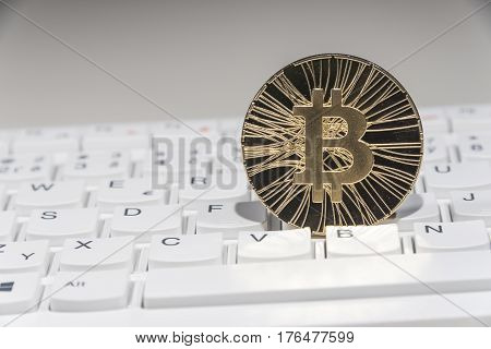 Shining gold metal BTC bitcoin coin on white computer keyboard.