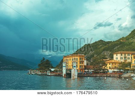 Beautiful retro toned cityscape of coastline of italian Varenna city with Como lake building big trees green mountain and dramatic sky before the rain