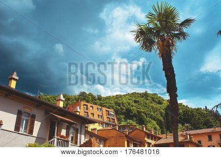 Beautiful toned cityscape of italian Varenna city with building big palm green valleys and dramatic sky before the rain