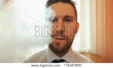 Young Funny White Businessman With Beard And Mustache Emits Puff Of Steam From The Electronic Cigare