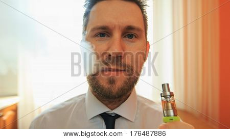 Vape. Young Funny White Businessman With Beard And Mustache Emits Puff Of Steam From The Electronic