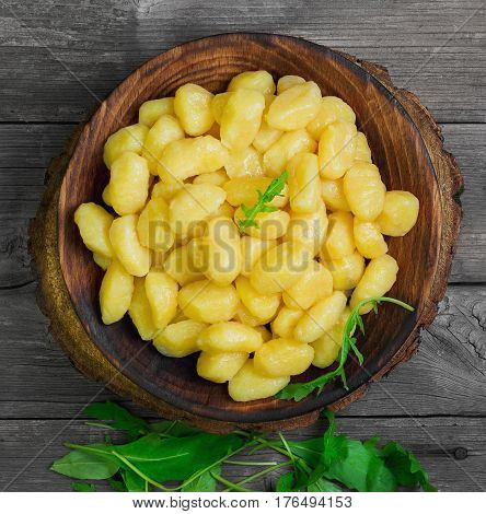Homemade Potato dumplings Gnocchi in wooden plate. On gray wooden table background ingredients for Potato dumplings Gnocchi Salad of rucola fresh green onion sauce forks.