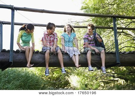 Cuatro adolescentes 916-17 años) sentado en el puente de madera, hablando, sonriendo