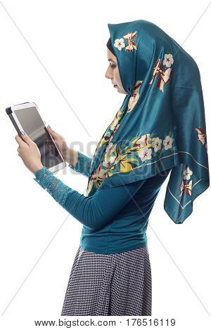 Female wearing a green hijab reading news online on a tablet or social networking via mobile device. She is isolated on a white background. The conservative outfit is associated with muslims and middle eastern culture.