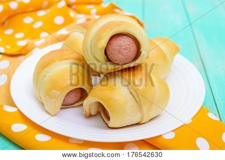 Freshly baked small buns on a white plate. Sausage in the dough.