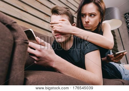 Disgruntled girl closes eyes to her boyfriend who flirts in the phone on a dating site