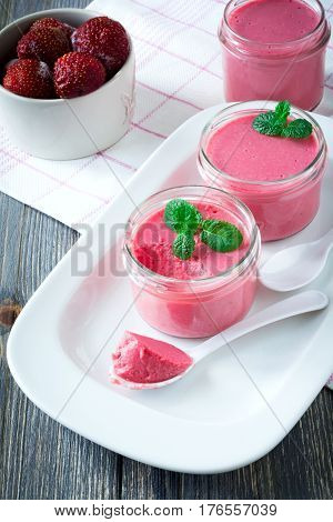 Strawberry mousse in glass jars and frozen strawberries on an old wooden table background. Selective focus.