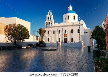 Picturesque square and white church of Panagia Platsani with blue dome in Oia or Ia on the island Santorini in the morning, Greece