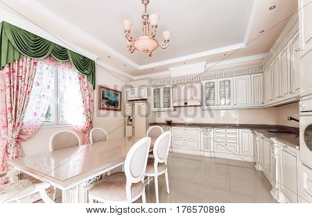 Large comfortable kitchen. In the middle of the kitchen a massive wooden table in the style of Classicism with a marble surface. Beautiful kitchen furniture and marble floors.