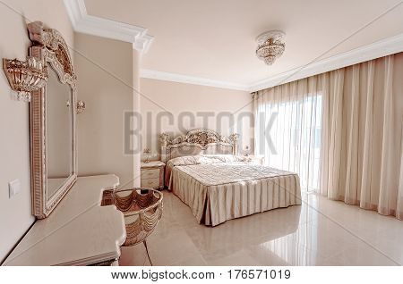 Luxurious bedroom in pastel colours in a neoclassical style with a large bed and a dressing table with marble floors.