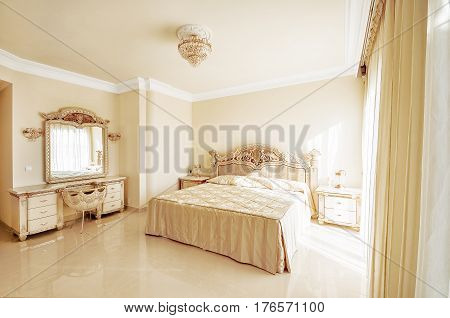 Luxurious bedroom in pastel colours in a neoclassical style with a large bed and a dressing table with marble floors.