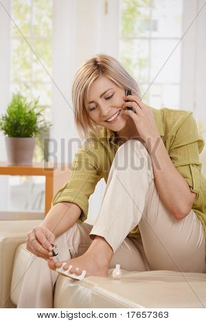 Gülümseyen kadın evde kanepede otururken ayak tırnak cilası kullanırken cep telefonda konuşurken.?